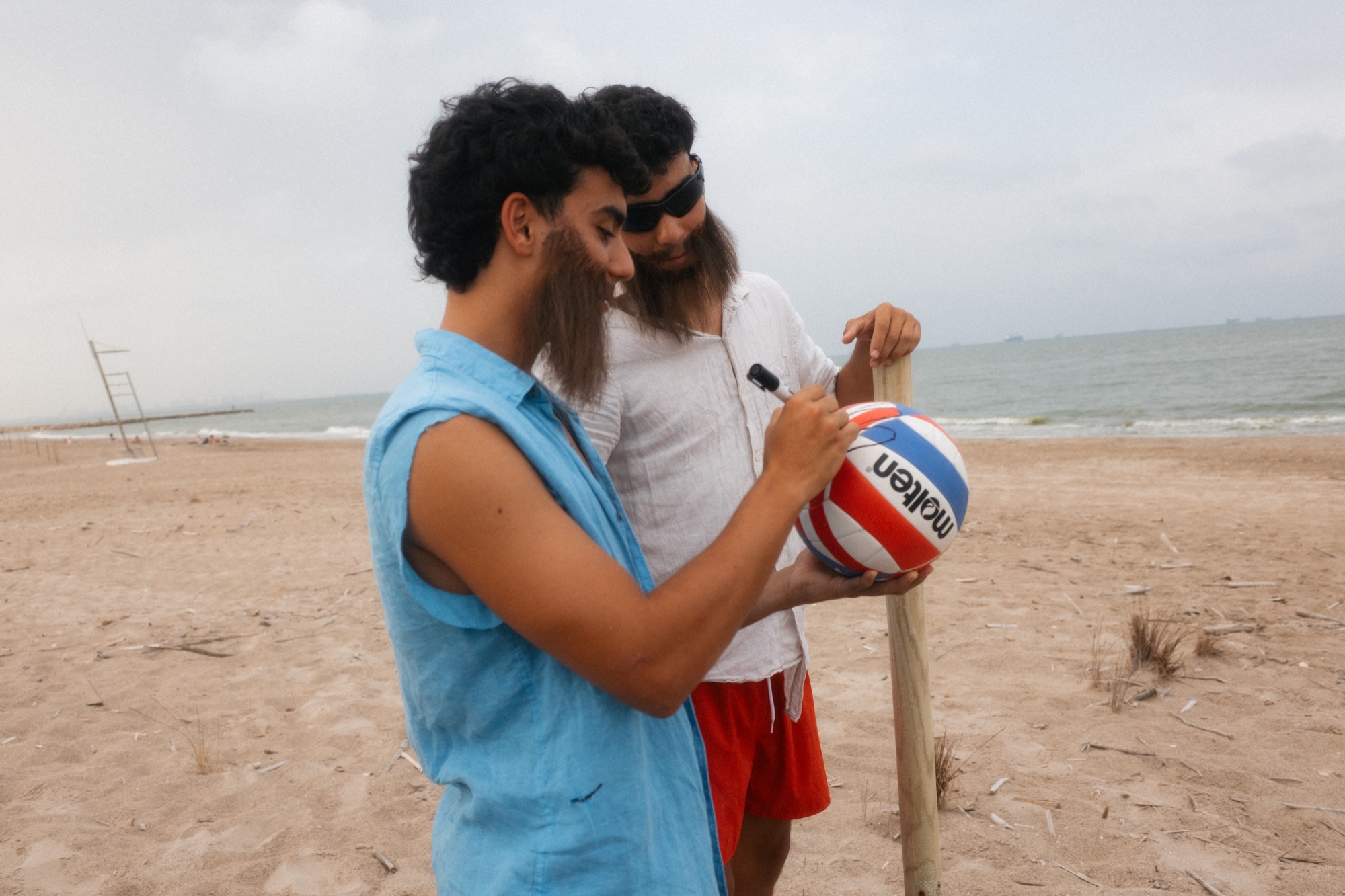 Los Sepuls caracterizados como náufragos dibujan sobre una pelota de vóley en la playa